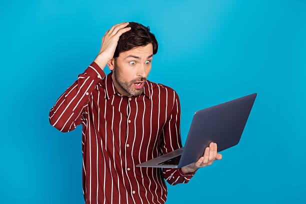 istock Young man with laptop shows surprised expression on blue studio background for an advertising lifestyle image 2247102620