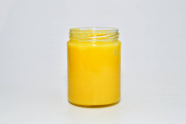 Yellow ghee in a glass jar on a white background.