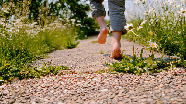 A young toddler joyfully exploring a backyard footpath with blooming daisies, walking barefoot and embracing the sunny day in a playful manner.