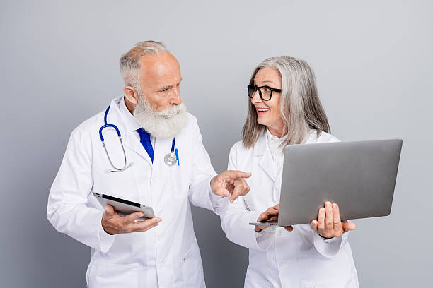 istock Two aged doctors discuss patient care using tablet and laptop in a clinic setting with stethoscope and glasses 2247107185