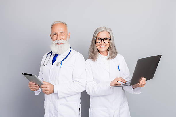 istock Two doctors aged and experienced colleagues in white coats stand in a clinic using tablet and laptop for medical consultation and patient care 2247107222