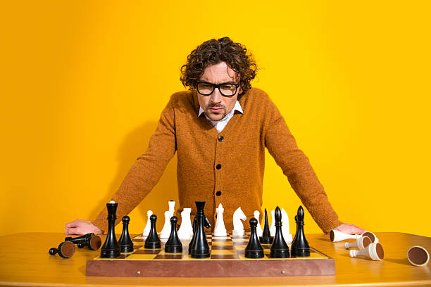 istock Young man in orange cardigan plays chess at bright yellow backdrop with scattered pieces 2247107939