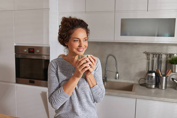istock Happy woman drinking coffee smiling in kitchen 2247108586