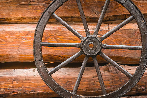 istock Vintage wooden wagon wheel resting against a rustic log wall in a warm, cozy setting 2247111148