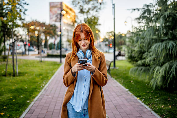 istock Young woman walking outdoors checking smartphone in city park 2247111189