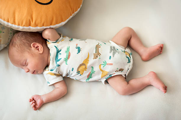 istock Baby sleeping peacefully on soft surface surrounded by colorful dinosaur-patterned onesie and plush cushion 2247113530