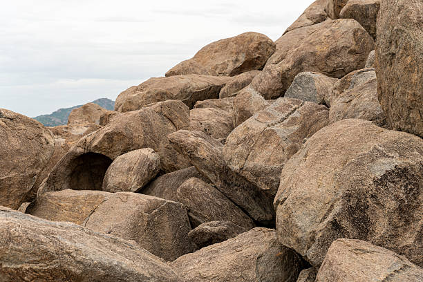 A pile of rocks with a few holes in them. The rocks are grey and brown. The pile is on a hill. Tamil nadu