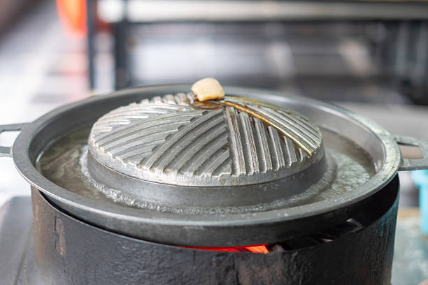 Close-up of Thai-style barbecue grill pan, known as Moo Kratha, with pork belly, shrimp, and vegetables cooking on a hot grill and soup. Popular Asian dining experience in Thailand.
