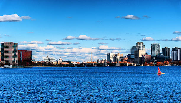 View over the Charles River of the Boston skyline including the Longfellow Bridge extending from Cambridge to Boston's Beacon Hill neighborhood. The bridge is also known as the Salt-and-Pepper Bridge due to the shape of its central towers. A Zakim Bunker Hill Memorial Bridge tower is seen in the center background. Two boats are sailing on the river.