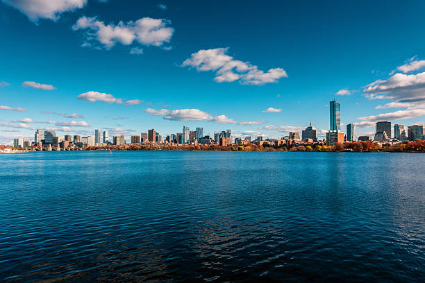 View over the Charles River of the Boston skyline extending from the Longfellow Bridge's start in Cambridge on the left, over Boston's Beacon Hill and downtown districts, and westward through Boston's Back Bay neighborhood. A single sailboat is sailing on the river.