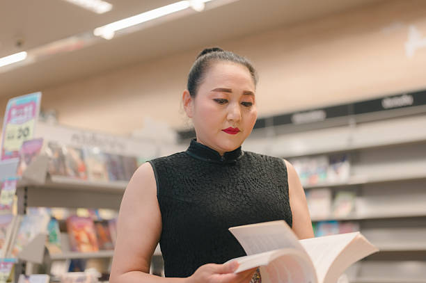 istock Mid Adult Woman Reading Book in Store with Focused Expression 2247123023
