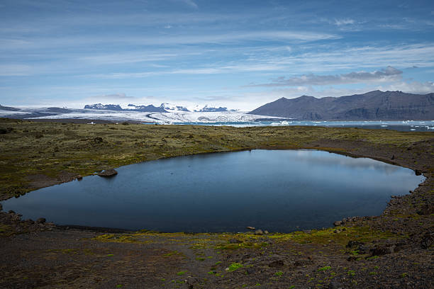 Moss-covered terrain meets a calm lake before glacier lagoon and mountains.
