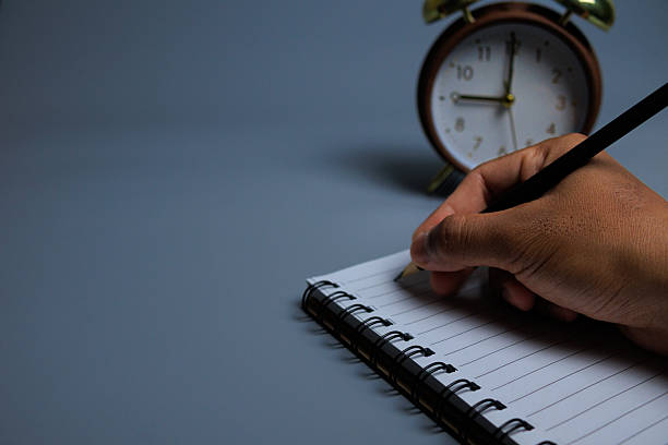 istock A calm scene showing a hand writing in a spiral notebook with a classic alarm clock 2247124951