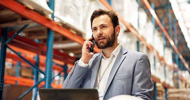 istock Supply chain, phone call and man in warehouse, distribution and schedule for cargo shipping. Person, laptop and employee in workplace, smartphone or logistics with delivery checklist or communication 2247125578
