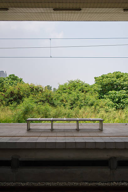 istock Empty bench on a train station platform facing green trees, with overhead wires and blue sky in the background. 2247128937