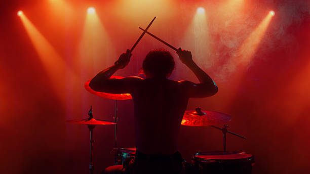 istock Drummer silhouette under orange light raising drumsticks in emotional finale 2247133007