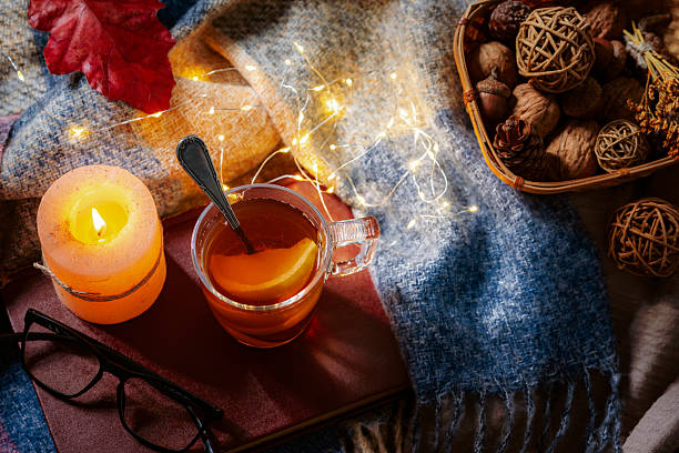 Cup of hot herbal tea in a cozy Autumnal decorated table. Candle, walnuts or blanket