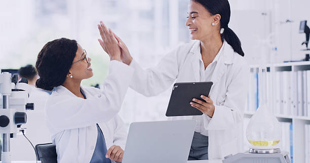 istock Tech, research and women with high five, science and cure with medical study, app and support. Achievement, people and scientists in lab, laptop and tablet with gesture, teamwork and new discovery 2247134930
