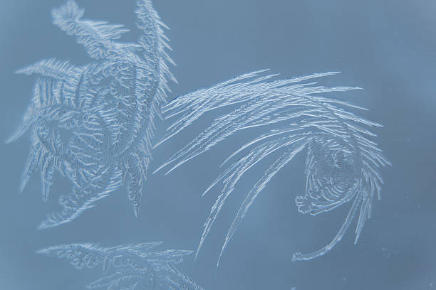 Frost patterns create delicate, intricate designs on a glass surface,..
