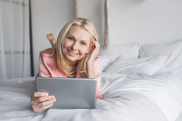 istock Woman, tablet and browsing internet in bedroom, morning with e-book, working online. Middle age female person happy to relax in bed with digital touchscreen for streaming app at apartment copy space 2247137142