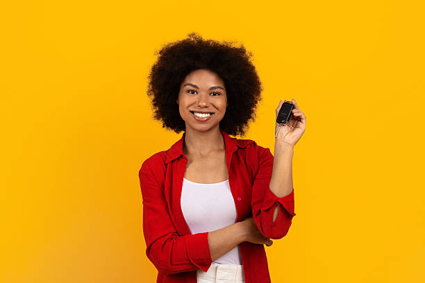 istock Smiling black woman holding car key and standing against yellow studio background 2247138097