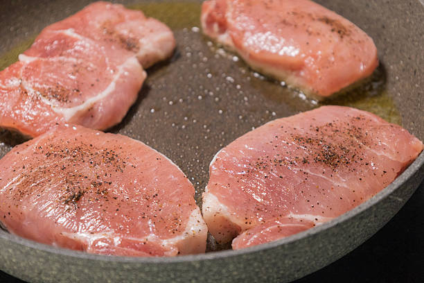 close up of raw pork chops seasoned with salt and pepper placed in a pan ready to cook. perfect for recipe preparation, kitchen scenes, meat cooking tutorials, meal prep visuals, and culinary content. ideal for butcher themes, protein dishes, and home cooking photography.
