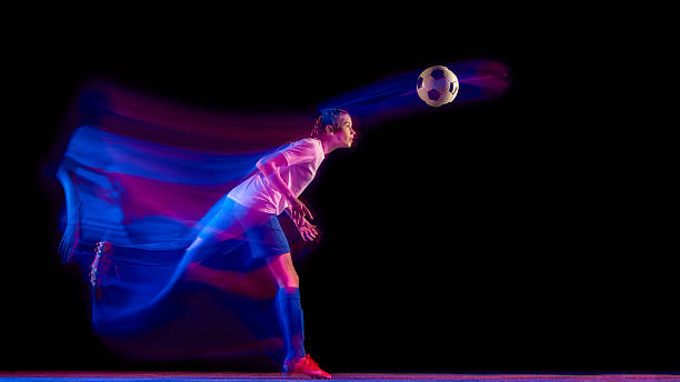 istock Female football player heading ball under glowing studio light. 2247140418