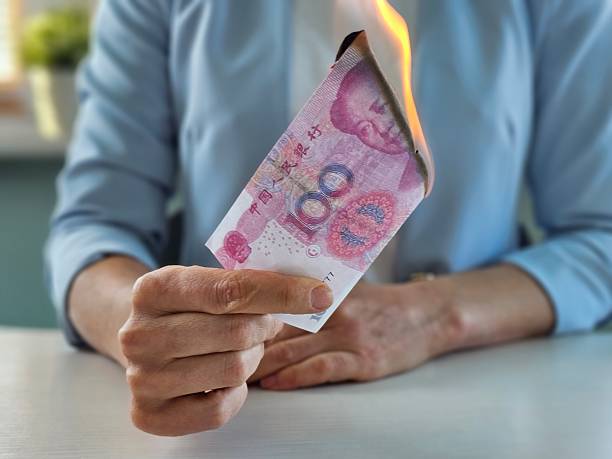 istock A person is holding a burning Chinese yuan note, showing a worried expression 2247145758