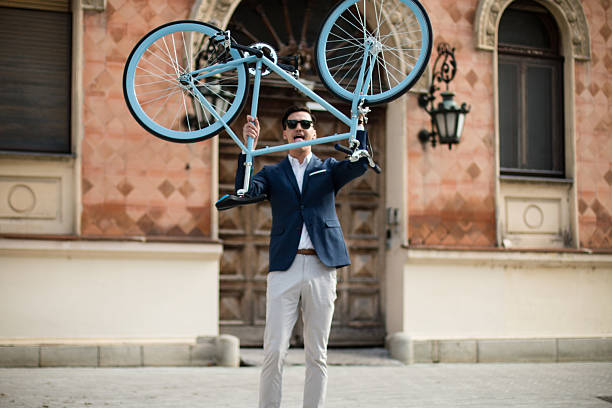 Portrait of a young happy businessman in suit on the street holding up his blue bicycle