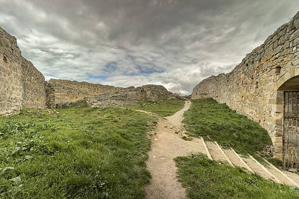 Stone ruins of a medieval castle on a grassy hill with cloudy sky in Aguilar de Campoo, Spain.
