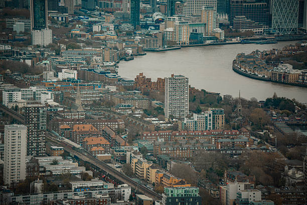 Aerial view from Bishopsgate in the City of London showing the corridor along Tower Hamlets including Rotherhithe, Whitechapel, Shadwell, Wapping, Limehouse, and Canary Wharf. Parts of Rotherhithe and the River Thames waters are also visible. Residential and commercial buildings, streets, docks, and office towers are visible.