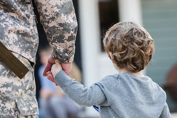 istock Child holds military parent's hand, symbolizing connection and return home. 2247155016