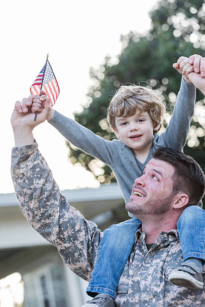 istock Proud soldier carries son on shoulders, both waving a small American flag. 2247155021