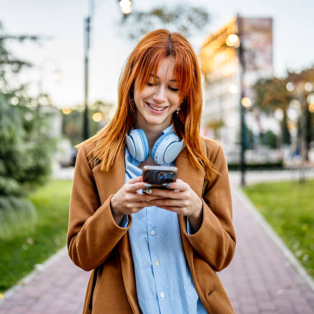 istock Young woman smiling while texting on smartphone outdoors 2247155632