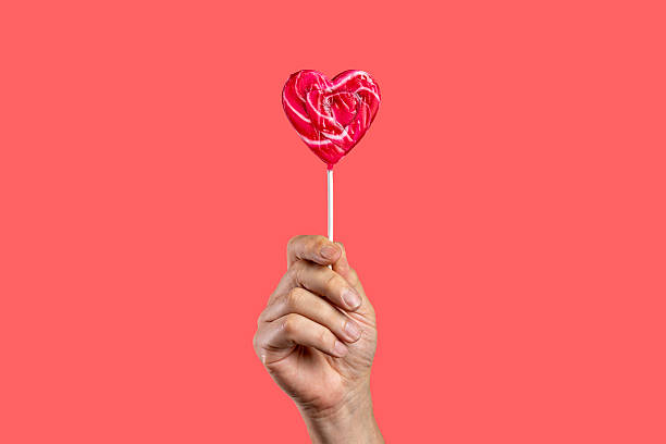 istock Hand holding a heart-shaped lollipop on a vibrant pink-red background. 2247158363