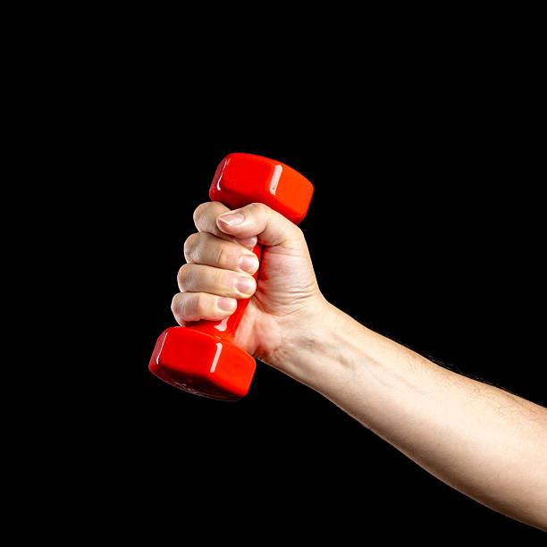 A man's hand holds a red dumbbell, gripping it tightly for a strength training workout, isolated on a solid black background.