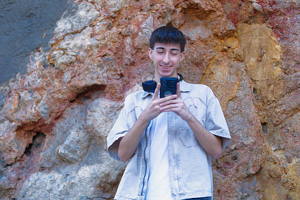 A young Gen Z man wearing large over-ear headphones checks his smartphone while standing in front of a colorful, vibrant wall