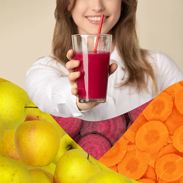 Food, ABC, health care, wellness concept. Beautiful woman holding in front of the camera glass of red juice with straw made of apple, beetroot and carrots. Vegetables and fruits in foreground