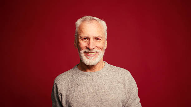 istock Portrait of happy senior man touching grey beard looking at camera posing isolated on red background 2247166985