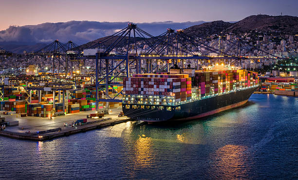 A illuminated, large container super cargo ship is being unloaded and loaded by cranes and trucks