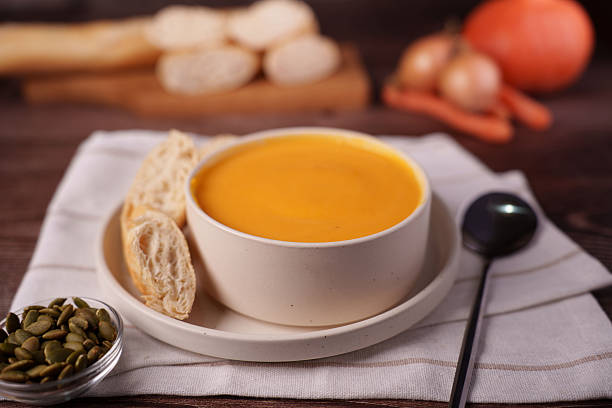 istock cozy autumn setup featuring a creamy pumpkin soup in a white ceramic bowl accompanied by slices of rustic bread, pumpkin seeds, and a spoon on a wooden table with soft focus background, texture 2247173855