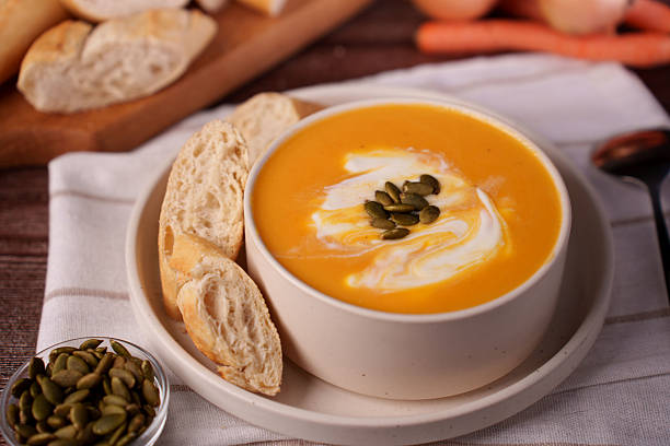 istock cozy autumnal setting featuring a creamy pumpkin soup garnished with seeds and accompanied by rustic bread slices, evoking warmth and comfort with its rich and vibrant presentation, presentation 2247173873