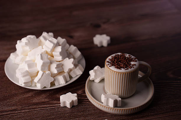 ceramic cup with frothy cappuccino topped with chocolate sprinkles beside a plate of star-shaped marshmallows on wooden table setting a warm cozy atmosphere, moment, peaceful, scene, tabletop