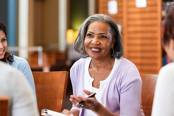 istock Elderly woman in group therapy session, smiling and gesturing with a pen 2247174159