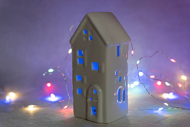 istock Small white porcelain house illuminated by colorful festive string lights, creating a cozy holiday atmosphere 2247174397
