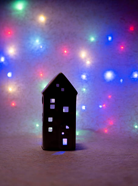 istock Ceramic house decoration with bright windows, set against a blurred background of colorful Christmas string lights 2247175177