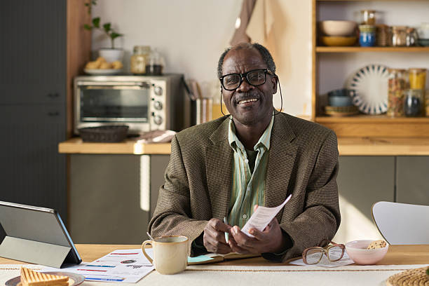 istock Portrait of Senior Black Man Smiling While Reading Documents at Table 2247175235