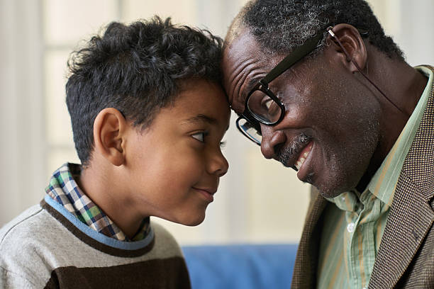 istock Senior Black Man Smiling While Touching Forehead with Boy Indoors 2247176164
