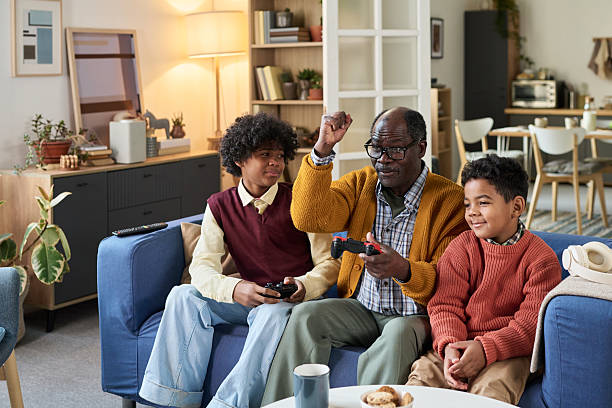 istock Mature Black Man Playing Video Game with Two Black Boys on Sofa 2247176985