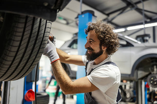 istock Mechanic smiling while inspecting car tire in garage 2247184236